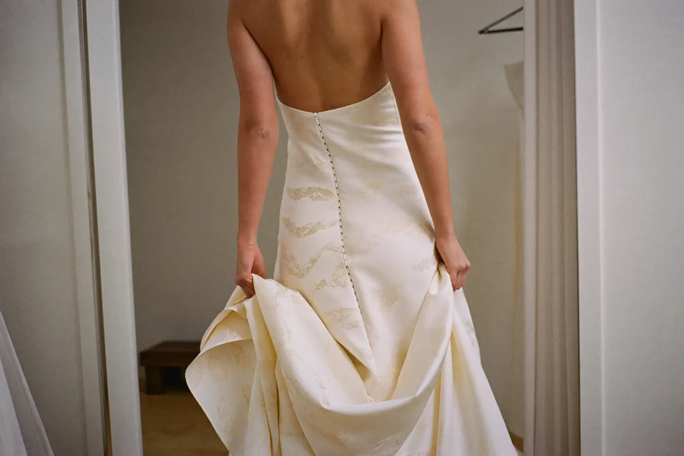 Anprobe eines asymmetrischen Brautkleids mit schrägem Saum, Braut von hinten im Atelier