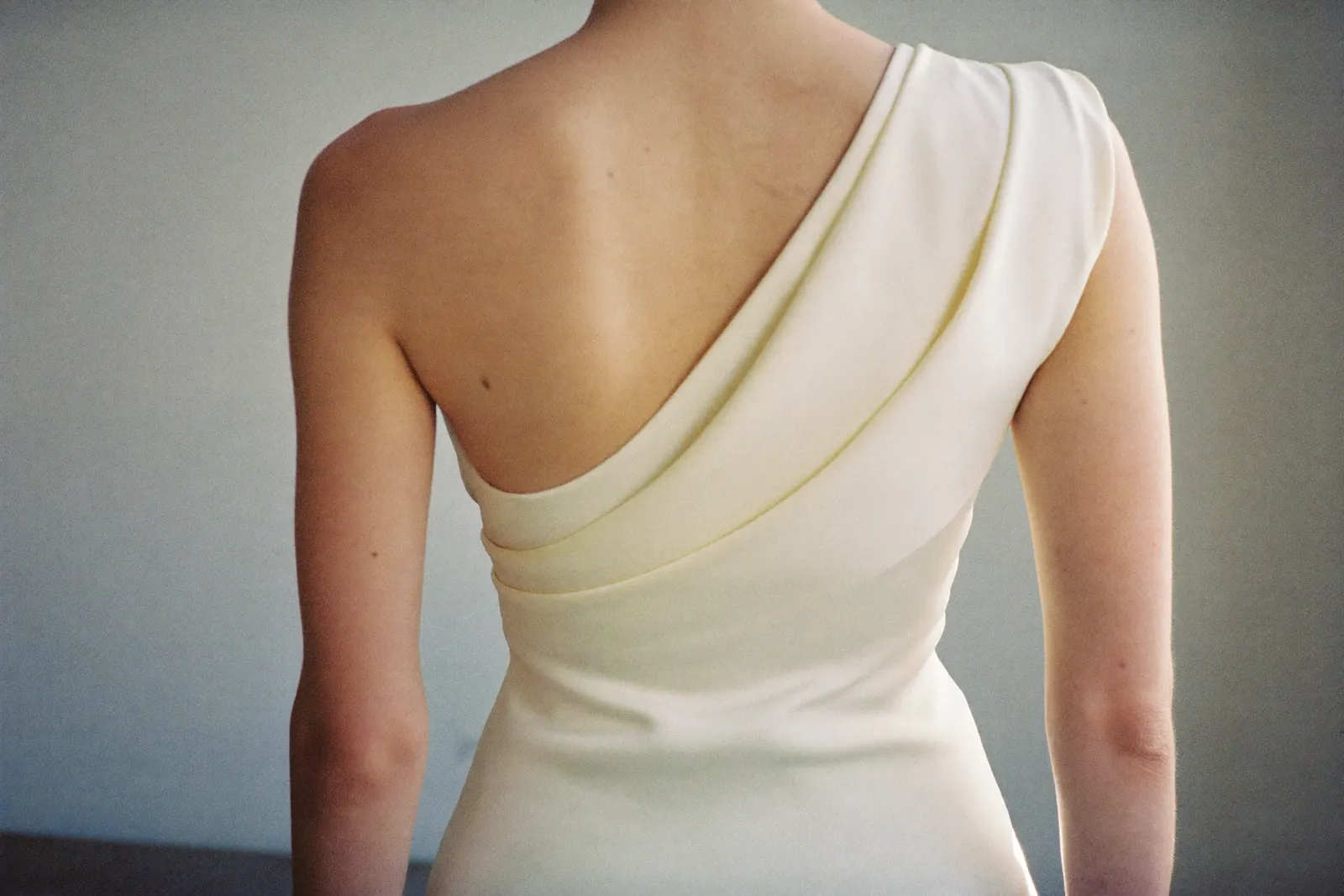 Asymmetrisches Brautkleid mit One-Shoulder-Träger und diagonaler Drapierung, Braut von hinten in warmem Tageslicht