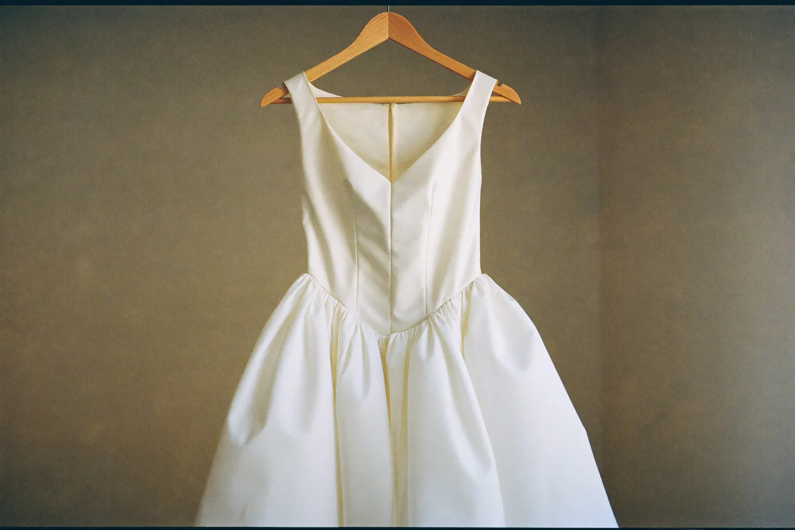 Designer Brautkleid auf einem Bügel im weichen Tageslicht, feiner Stoff im Detail, ruhige Atmosphäre
