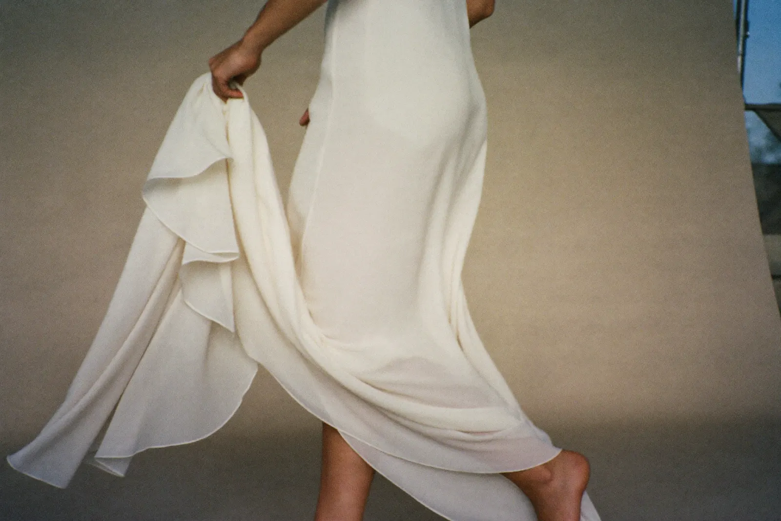 Fließendes Brautkleid aus leichtem Chiffon in Bewegung, Braut von hinten in warmem Tageslicht