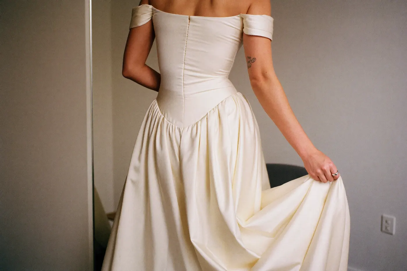 Braut im Off-Shoulder Brautkleid von hinten bei der Anprobe mit fließendem Rock