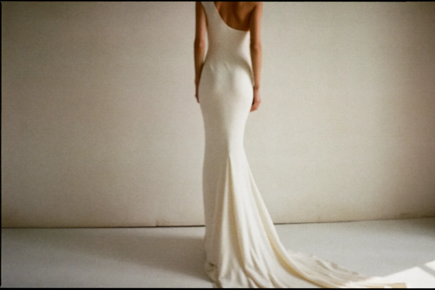 Braut im schlichten One-Shoulder Brautkleid aus Crêpe von hinten im Atelier