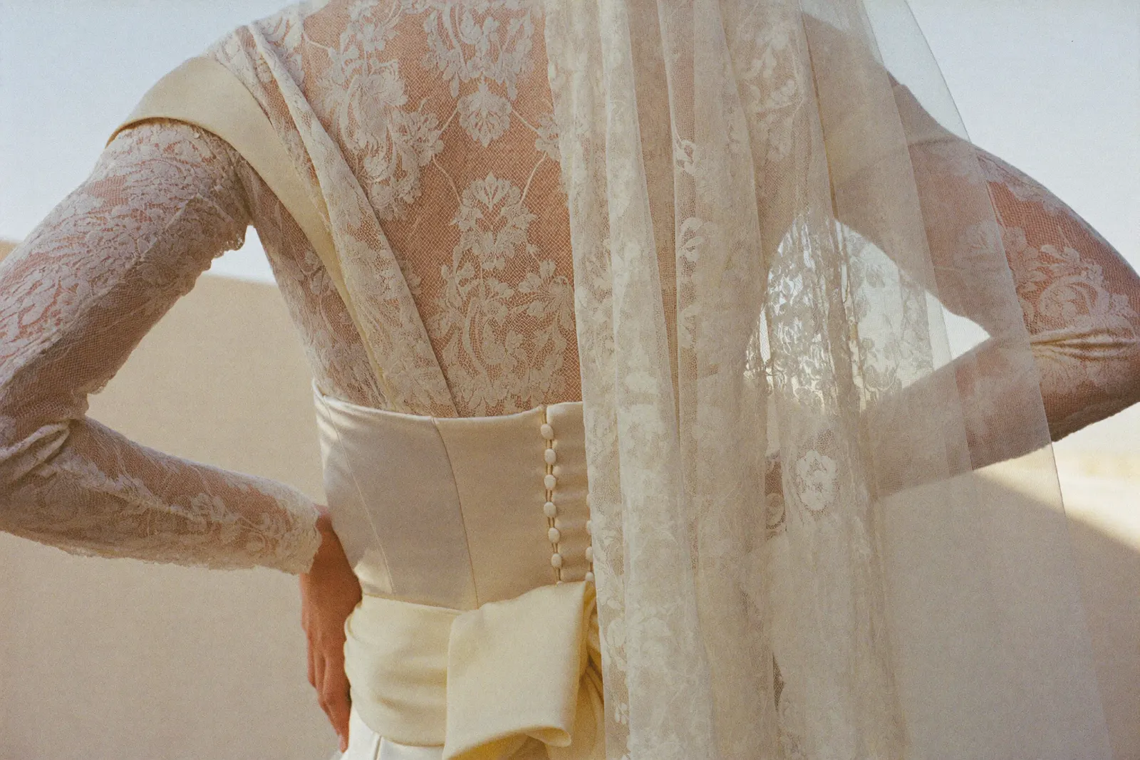 Vintage Brautkleid aus feiner Spitze in weichem Tageslicht, Stoff im Vordergrund, Braut im Mittelpunkt
